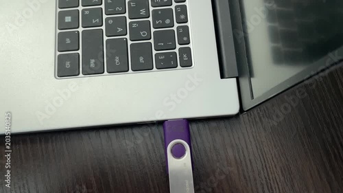 Attaching purple storage device to laptop port. Inserting portable flash drive into computer for file transfer. Connecting purple removable media device to laptop port for data transfer and backup