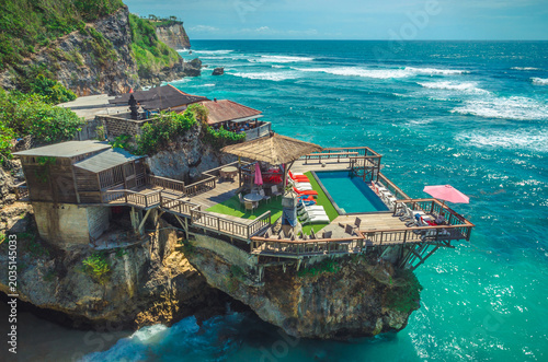 Beautiful Uluwatu coast with rocks and ocean waves, Bali, Indonesia. Swimming pool on the terrace above the ocean.