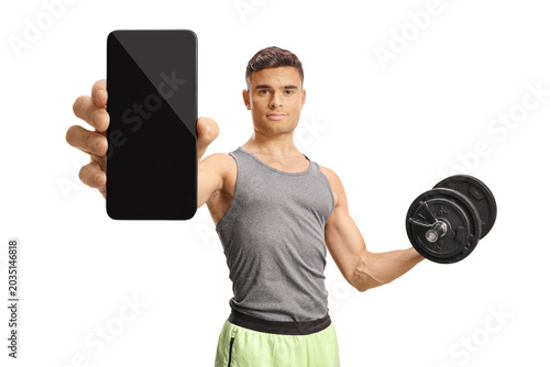 Young man holding a dumbbell and showing a smartphone with blank screen