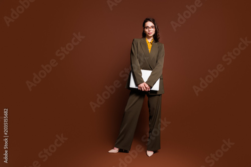 Tableau sur toile Confident professional woman in olive pantsuit holding a laptop, modern corporat