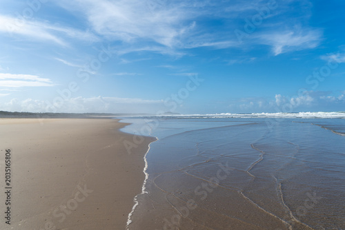 Tableau sur toile Ocean waves washing onto a sandy shore, with visible ripples, in the late afternoon