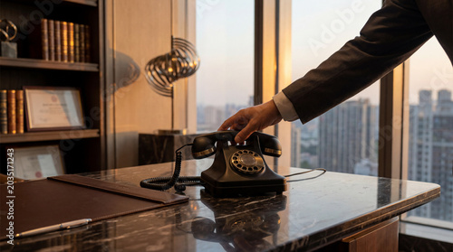 Hand reaching for vintage rotary telephone on a wooden desk in a business office