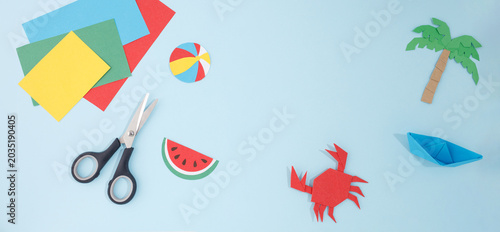 Summer paper crafts elements on blue background with copy space. Scissors, origami crab, boat, palm tree, watermelon. Ideal for kids education centers, summer camps, kindergarten marketing.