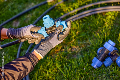 Closeup of hands in the gloves. Process of plumbing, installing fittings pipes and connectors for the garden and lawn irrigation system installation. Green grass, shallow depth of field.