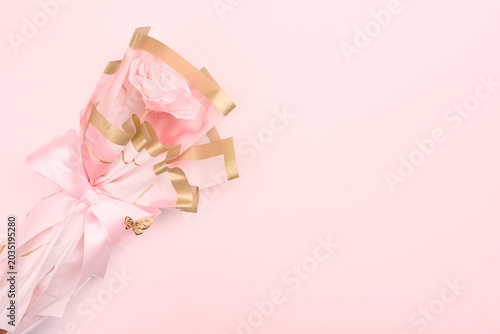 Pink fabric rose wrapped in decorative floral paper with a bow on a pink table. Copy space. 