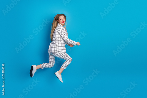 Foto Happy young woman jumping in checkered suit on a bright blue background conveyin
