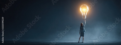 Woman holding a bright idea lightbulb aloft against a dark, smoky background