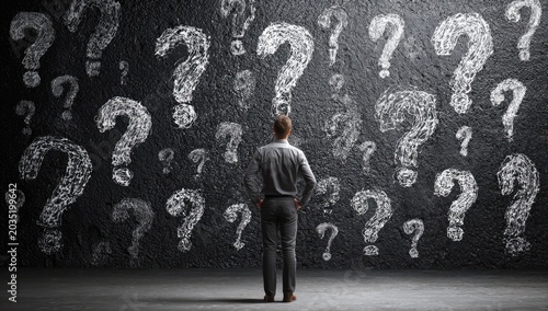 Man faces wall covered in chalk question marks, pondering life's mysteries