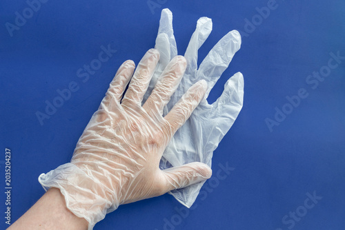 Human hand wearing transparent disposable plastic gloves isolated on blue background. Hygiene, healthcare, and protection concept.