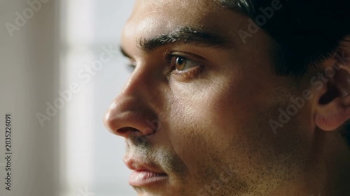 Camera recording man tilting head, parting lips, tracking left near window, catchlight and stubble
