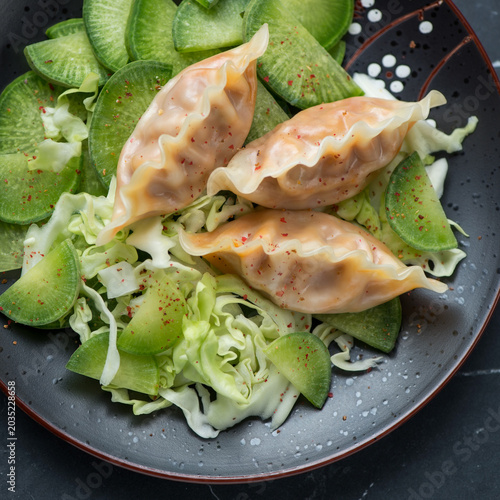 Asian steamed dumplings with fresh cabbage and green radish served on a black plate, close-up, high angle view