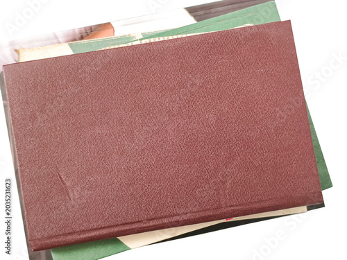 A brown hardcover book rests on top of a stack of other miscellaneous books, isolated on white.