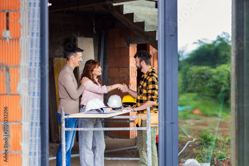 Foto Adult couple making agreement with handshake with a contractor at a house construction site