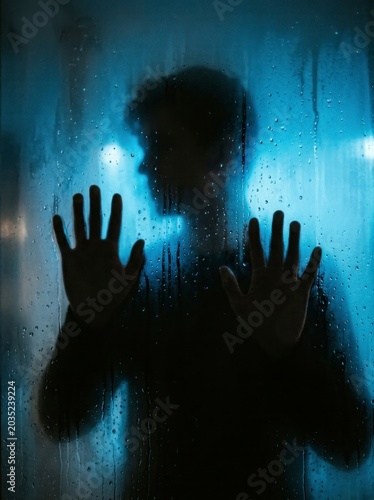 Silhouette of a person behind wet glass, blue mood.