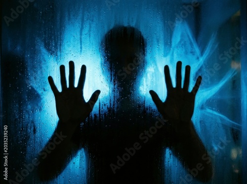 Silhouette of a person behind wet glass, blue light.