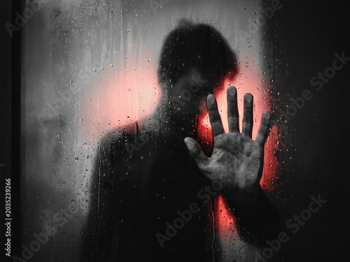Silhouette of a person behind wet glass, red backlight.