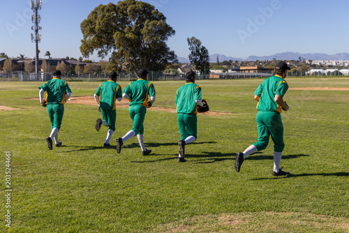 Tableau sur toile Five baseball players jogging across grass outfield, warmup drill starting glove