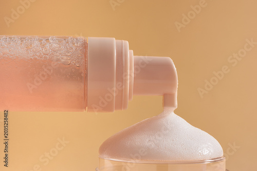 Fotografía A close-up of a pink foaming skincare cleanser being dispensed from a pump bottle against a soft beige background