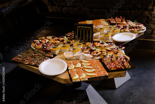 A catering buffet table filled with an assortment of gourmet appetizers, including salmon canapes, meat rolls, bruschettas, and mini desserts at an event.