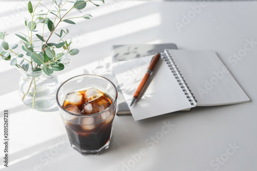 Photography Iced coffee and notebook on bright minimal workspace with eucalyptus