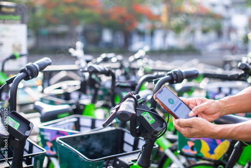 A close-up shot of hands holding a smartphone to scan a QR code on a blue shared bicycle's handlebars, unlocking it for a ride on a blurred city street.