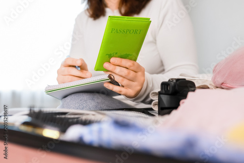Fotografie Woman writing a packing list and holding a green passport for travel preparation