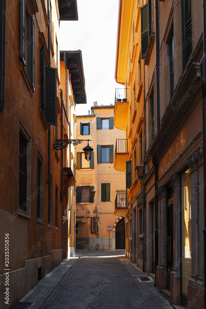 Fototapeta premium Narrow Cobblestone Alley Framed by Historic Warm Colored Buildings with Green Shutters in Verona Italy