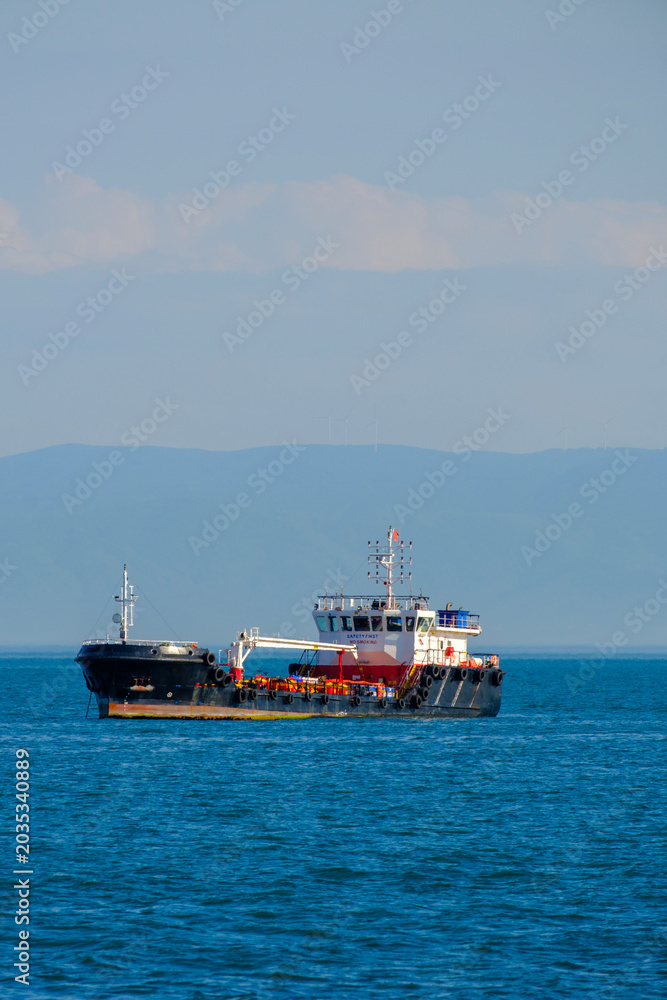 Fototapeta premium Small black and white coastal supply ship sailing against a clear sky