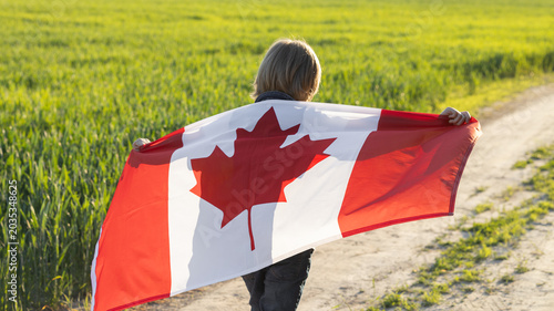 Foto unrecognizable child walks down a country road, holding a large Canadian flag behind him in the sunlight