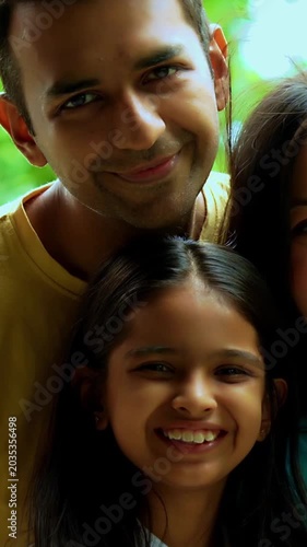 Indian parents with infant outdoors in garden, smiling while standing, looking at camera, showcasing happy family bonding, lifestyle, love, parenthood, outdoor portrait in natural greenery
