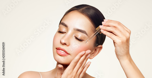 Young beautiful woman applying face serum with pipette. Cosmetic procedures for facial skin care