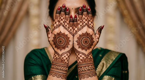 Close-up of a woman hands with beautiful traditional henna mehndi design on her wedding day, wearing an elegant green saree.