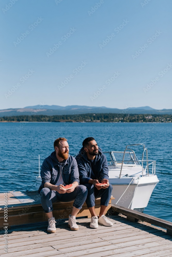 Obraz premium Two men sitting on a dock holding shells and looking at the sea for social media banner and travel background