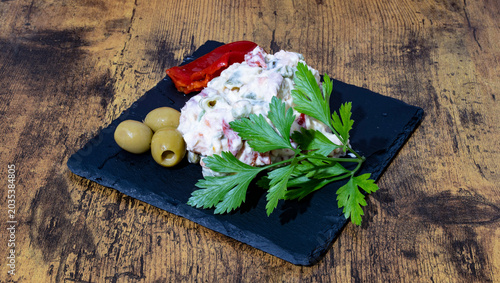 Photos Ensaladilla Rusa Casera, con hoja de perejil, olivas rellenas y pimientos del piquillo sobre una plato de pizarra negro