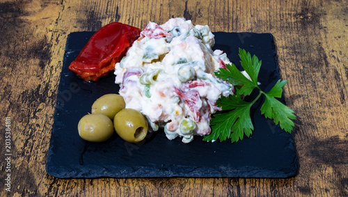 Photos Ensaladilla Rusa Casera, con hoja de perejil, olivas rellenas y pimientos del piquillo sobre una plato de pizarra negro