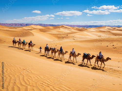 Camel caravan trekking across desert dunes under blue sky