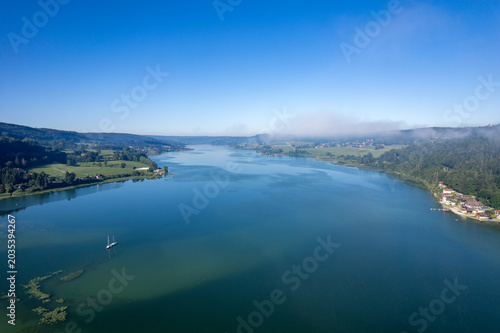 Lac jurassien vu par drone avec voile de brume et voilier solitaire
