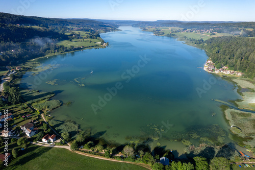 Lac jurassien vu par drone avec voile de brume et voilier solitaire
