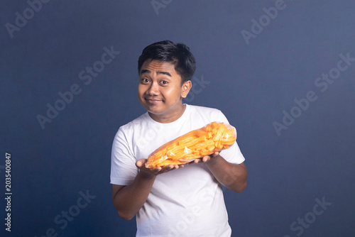 Schilderij op canvas Indonesian man in white t-shirt holding a large bag of orange snacks horizontall