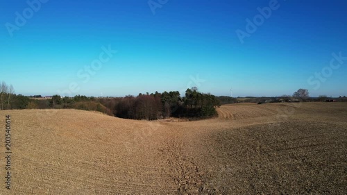 Forward drone flight over rolling farmland and woodland grove