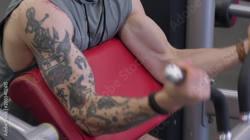 Man exercises arms at gym with focus on tattoos and workout equipment in action