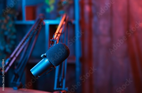 A modern podcast studio glows with vibrant hues as a microphone awaits interaction. Colorful lights reflect on the equipment, creating an inviting atmosphere for creative dialogue and exploration