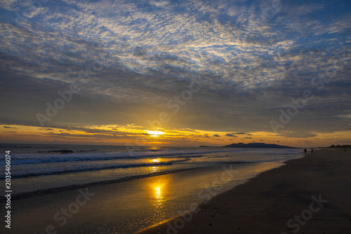 Golden sunset over tranquil beach with dramatic clouds and ocean waves, perfect for travel, tourism, vacation, nature, relaxation, coastal lifestyle, and scenic background use.