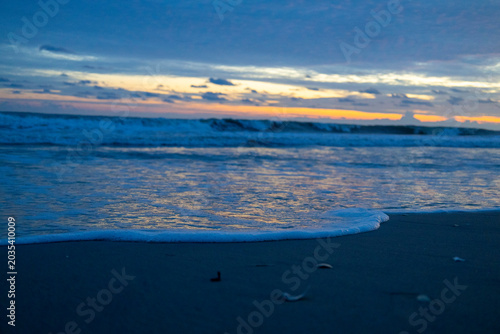 Peaceful ocean waves washing onto a sandy beach during a colorful sunset, perfect for travel blogs, tourism ads, relaxation themes, wallpapers, meditation content, and coastal lifestyle designs.