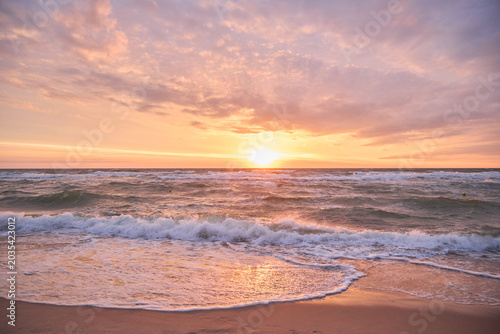 Beautiful marine landscape during a pastel sunset with calm sea waves washing sandy shore.