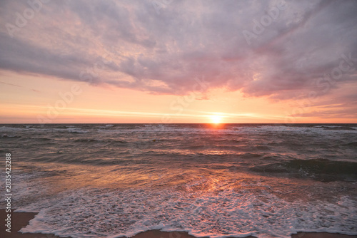 Close up of sea wave foam on a wet sand beach at twilight golden hour.