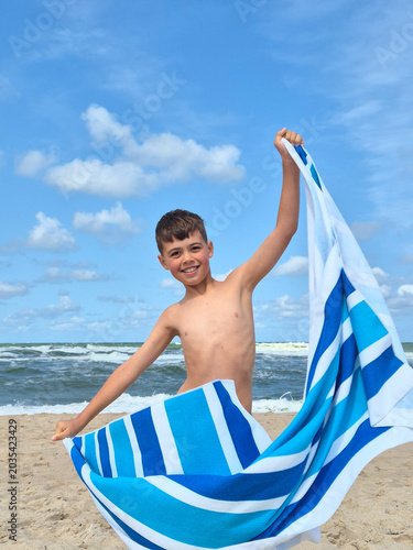 Joyful kid enjoying summer vacation on the seashore, blue sky background.