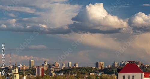 Kyiv, Ukraine - May 19, 2026: Scenic urban sunset skyline timelapse with fluffy cumulus clouds flying over residential buildings and a green city hill.