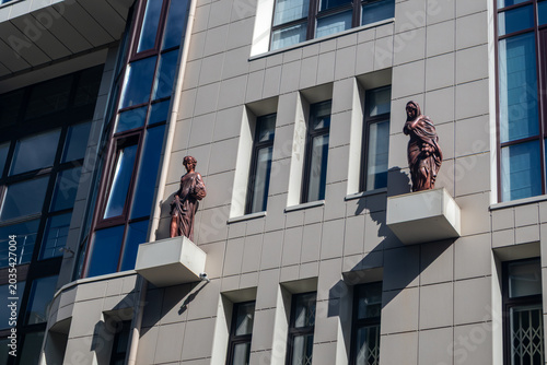 Modern building with two bronze statues of women on facade. Architecture details with visual contrast