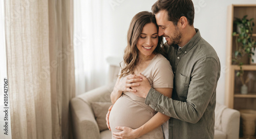 Happy smiling man hugging his pregnant wife from behind as she holds her baby bump.